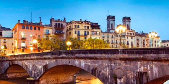 Stone bridge and lamplit riverfront houses in Girona at dusk